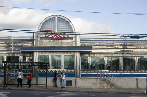 People wait for a bus in front of a shiny diner.