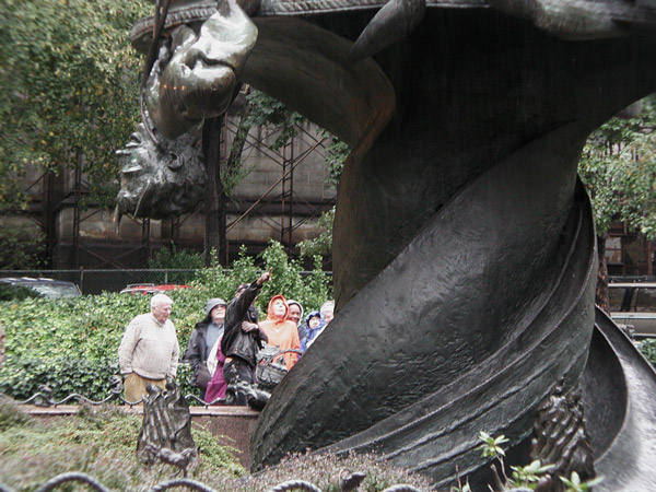 A tour guide points up to the details on a statue.