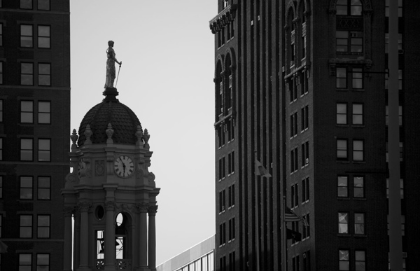 A statue stand on a dome with a clock, all in silhouette.