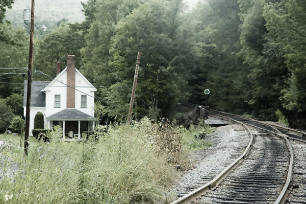 A white house sits near a curving railroad track.