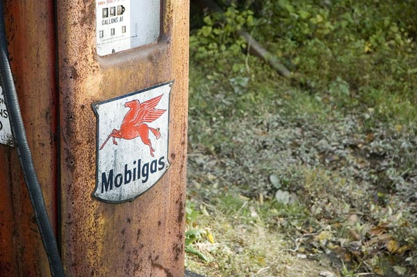 An old, red, rusting gas pump sits in a wooded area.