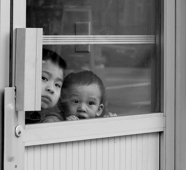 Two children peer through a glass door.
