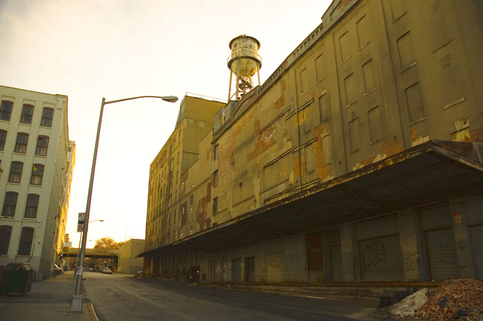 A water tank on top of an old warehouse, on an empty street.