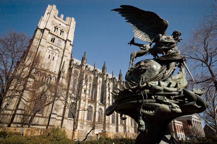 A sculpture depicts a battle between the archangel Michael and Satan. Behind it, a cathedral looms large.