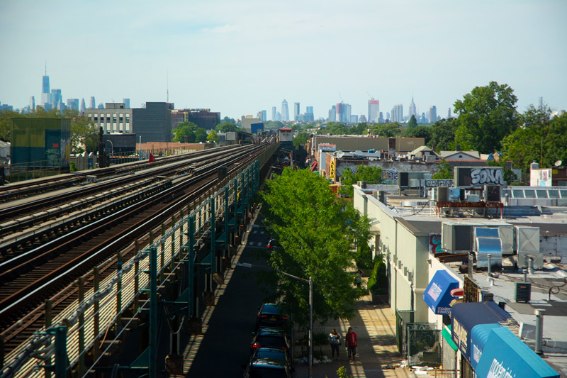 The photo shows elevated subway tracks, shortish buildings in Brooklyn, and the Manhattan skyline.