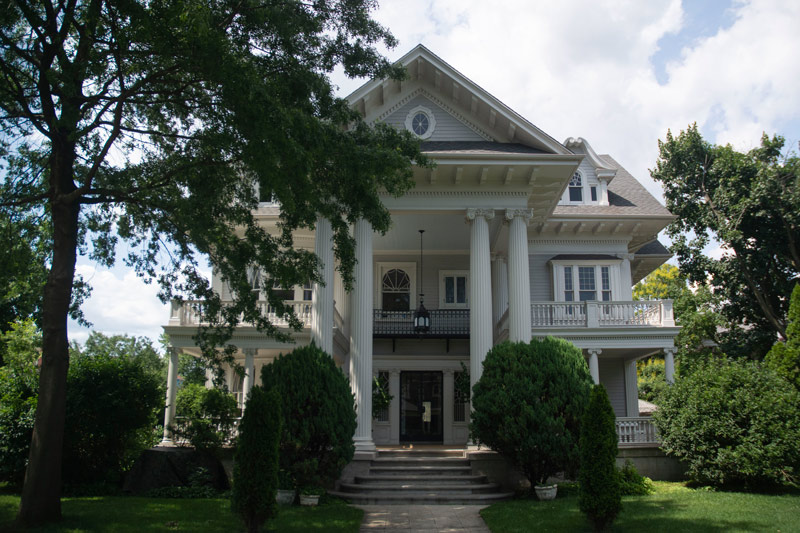 The photo shows a large two story house, with porches and balconies on all sides.