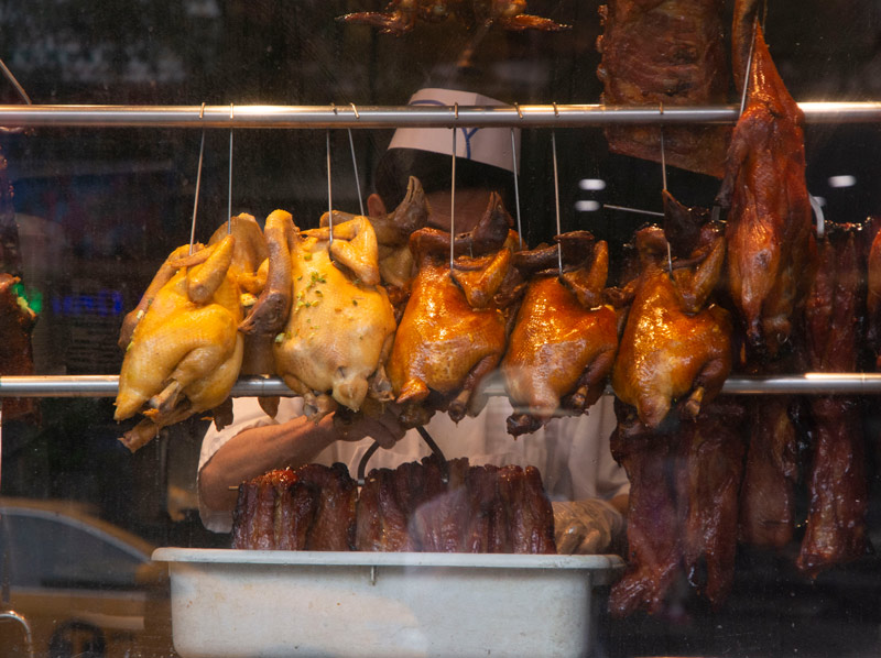 The photo shows a row of cooked ducks, hanging on a rack in a Chinese restaurant.