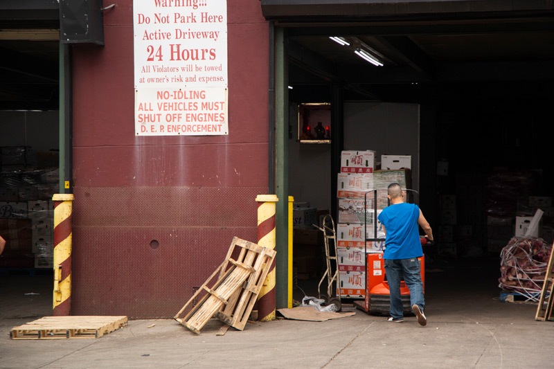 The photo shows a man moving crates of produce at a warehouse door.