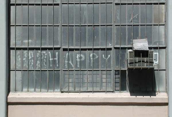 Grey warehouse
windows, with the word 'Happy' spray-painted on the panes.